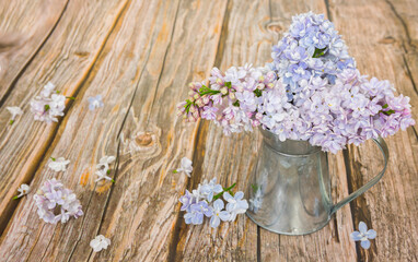 Branches of blooming lilac in a metal jug on a wooden background