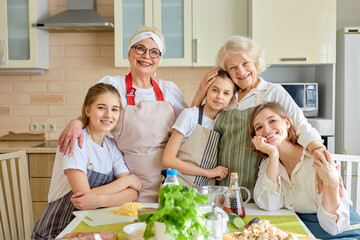 Cheerful women and kids of different generations enjoy being together at home, members of family...