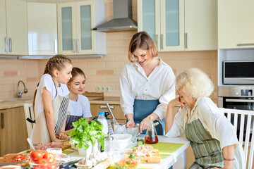 Young female making dough, teaching children to cook, going to make pizza, at home. Different generations females having talk, spending weekends together, looking at process of cooking