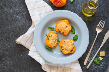 Stuffed yellow peppers with ricotta cheese and vegetables on a gray plate on a dark concrete background. Recipes for stuffed vegetables.