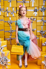 Funny little girl of caucasian appearance holding handbag in hands, looking up, wearing party dress. Children, party, birthday. celebration concept