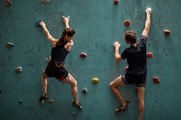Professional woman and man mountaineers climbing artificial rock wall with belay at bouldering gym,...