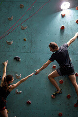 Confident woman and man mountaineers climbing artificial rock wall with belay at bouldering gym, in...