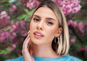 Young blonde Caucasian woman with lobbed haircut , beauty portrait in bloomed tree. Femininity and skin care concept 