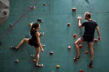 Athlete sporty woman and man in sportive outfit practicing rock climbing on artificial rock in...