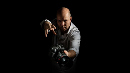 a man in a white shirt holds a camera in his hands on a black background