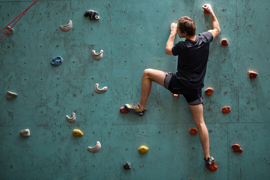 Caucasian man climber. Extreme indoor climbing. Strong man practicing climbing on artificial rock wall in sports club. Strong sporty male and male training speed bouldering session.