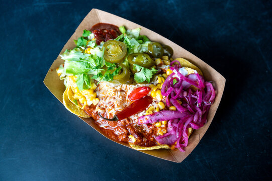 Chilli con carne in street food takeaway box with pickled onions, jalape&ntilde;os, parsley, corn and hot sauce.