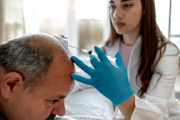 Fototapeta premium Cropped shot of a female beautician doctor makes injections in the man head for hair growth against hair loss and baldness. Doctor inject treatment serum vitamins to hair fall area on head by syringe.