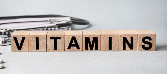 Vitamins inscription on wooden cubes isolated on white background, medicine concept. Nearby on the table are a stethoscope and pills.