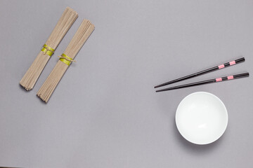 Dry buckwheat soba noodles, chopsticks, soup bowl.Flatlay on a gray background, horizontal, copy of the space
