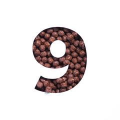 Number nine of chocolate cereal balls, white paper cut in shape of ninth numeral. Typeface for...