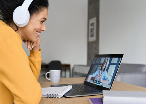 African American mixed race adult student wearing headphones having virtual meeting online call with teacher, educational webinar chatting at home office. Video e learning conference call on pc.
