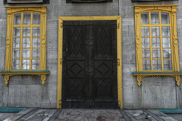 Yellow wooden platbands with carvings around windows and doors and a gray wall