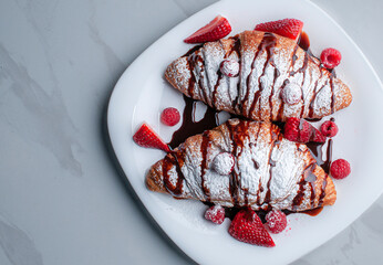 croissants or crossaints on a white plate with strawberries, raspberries, and sugar glass or candy glass with chocolate syrup on top copy space