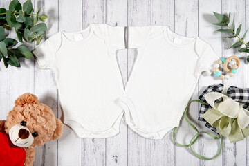 Baby wear two twins rompers onesie flatlay. On-trend farmhouse theme craft product mockup with farmhouse style decor, on a white wood background. Negative copy space for your design here.
