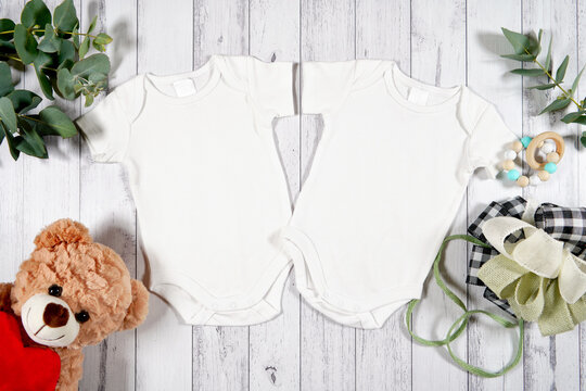 Baby wear two twins rompers onesie flatlay. On-trend farmhouse theme craft product mockup with farmhouse style decor, on a white wood background. Negative copy space for your design here.