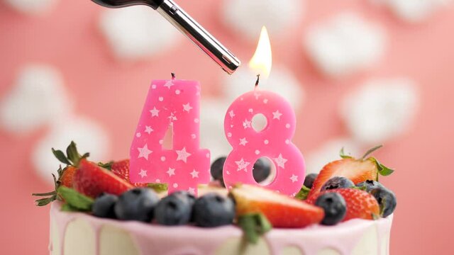 Birthday cake candle number 48. Candle and cake on pink background and fire by lighter. Close-up and slow motion