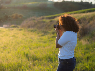 Mujer  joven morena de Honduras, con cabello rizado, fotografiando  el medio ambiente, en el  campo, rodeada de naturaleza verde, en un entorno rural y saludable, primavera de 2021