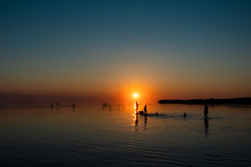 Silhouette of a big family walking on the lake at sunset. Concept of traveling family and enjoying the outdoors and the nature.