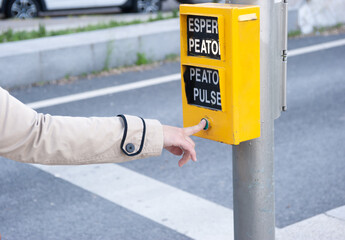 Woman's finger pressing the pedestrian button of a traffic light. The words that appear mean: "wait pedestrian", "press pedestrian".