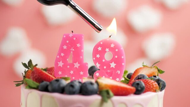 Birthday cake candle number 49. Candle and cake on pink background and fire by lighter. Close-up and slow motion