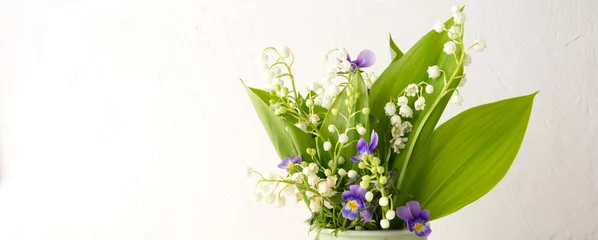 Rucksack delicate flowers lilies of the valley and violets in a green mug on a light table © kochabamba