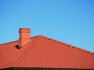 Red roof tiles with red brick chimney on blue sky background.
