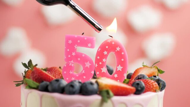 Birthday cake candle number 50. Candle and cake on pink background and fire by lighter. Close-up and slow motion