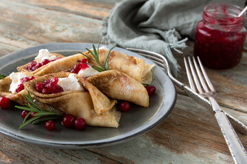 plate with thin pancakes stuffed with soft cheese with lingonberry jam and rosemary on a wooden...