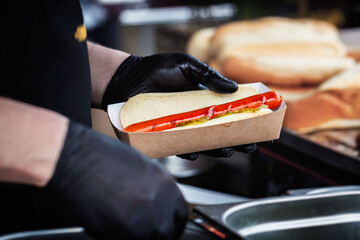 Hands of chef making fresh hot dog with vegetables and sauce. Fast food, Barbecue, grill concept