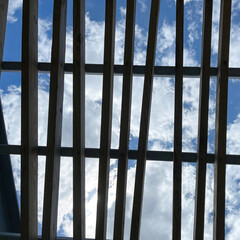 A wooden pergola roof at a park with bright blue skies and white  clouds.