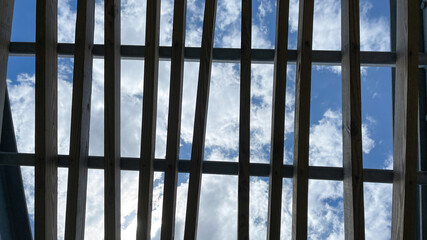 A wooden pergola roof at a park with bright blue skies and white  clouds.