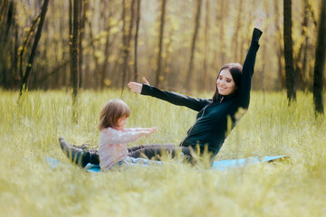 Cheerful Mother Exercising with her Child Outdoors on Yoga Mat