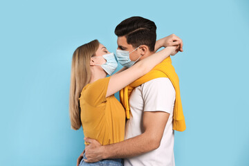 Fototapeta premium Couple in medical masks trying to kiss on light blue background