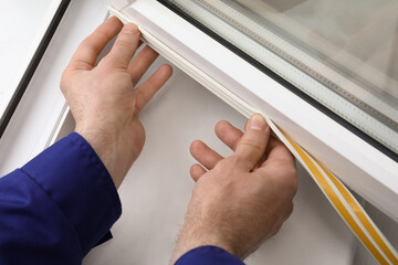 Worker putting rubber draught strip onto window indoors, closeup - obrazy, fototapety, plakaty
