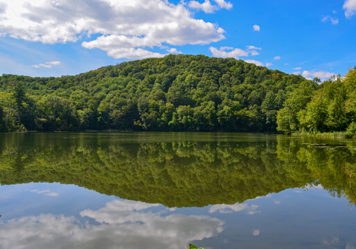 A lake in Vermont reflecting a wooded hillside and a blue summer sky with puffy clouds.  Copy space.