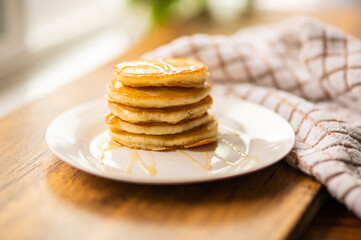 Pancakes with honey on a white plate on a wooden windowsill