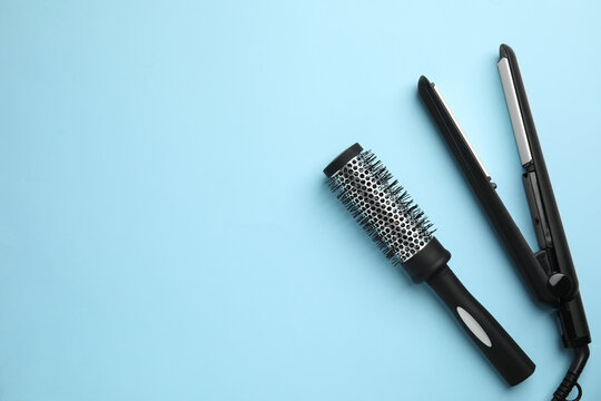 Hair straightener and round brush on light blue background, flat lay. Space for text
