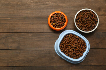 Obraz na płótnie Canvas Dry food in pet bowls on wooden background, flat lay. Space for text