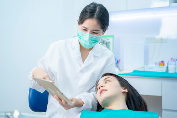 Asian female dentist wearing face mask, giving advice by using tablet.