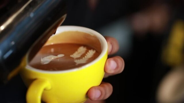 Close Up Barista pouring milk in coffee make rate art on top of hot coffee