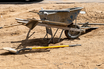 A dirty wheel barrow and other tools, used by a builder to make a concrete sidewalk at a construction job site.