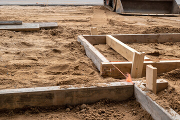 A wooden form for cement placement in the brown dirt at a construction job site. Two by four...
