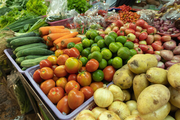 Red tomatoes are placed next to lemons, potatoes, cucumbers, carrots and broccoli on the stalls.