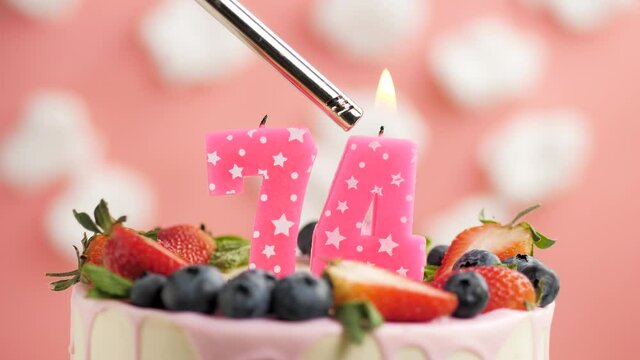 Birthday cake candle number 74. Candle and cake on pink background and fire by lighter. Close-up and slow motion