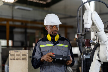 Male engineer holding robot controller for maintenance or repair automatic robotic machine in...