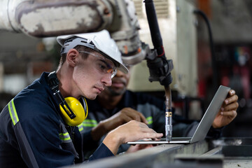 Male engineer worker working with computer notebook for control automatic robotic arm machine in...