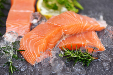 Fresh salmon fish on ice, Raw salmon filet with lemon rosemary herbs and spices on black plate