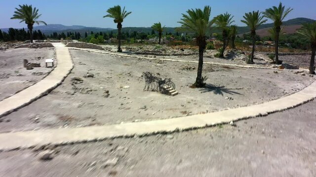 Aerial Shot Of Palm Trees At Tel Megiddo By Houses, Drone Flying Forward Over Protected Site Against Sky On Sunny Day
